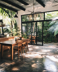Fototapeta premium warm, cozy interior featuring wooden dining table, surrounded by lush greenery and large windows. Sunlight filters through, creating serene