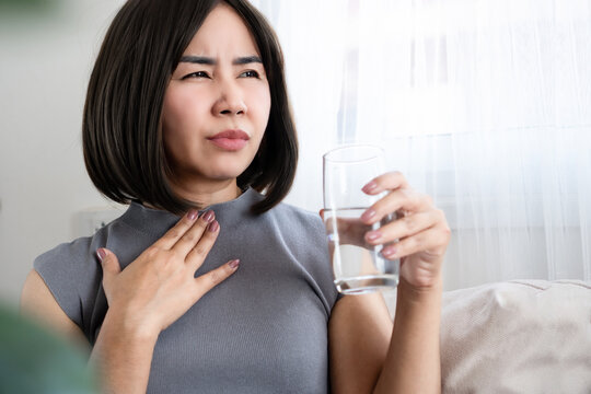 Asian woman experiencing sore throat, common cold symptoms, and difficulty swallowing while drinking water