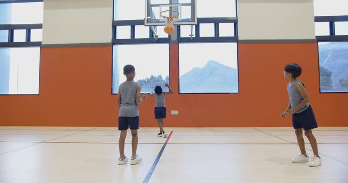 Playing basketball in school gym, three boys practicing dribbling and passing