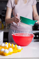 Making cupcakes at home. A woman prepares Easter cakes in the kitchen, pouring flour through a sieve.