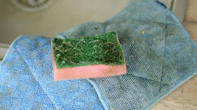 Tilt down close-up shot to a dirty kitchen sponge laying on the countertop by the sink. Blue dirty cleaning cloths.