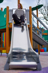 Adult woman sliding down a childrens slide enjoying life.