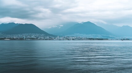 Serene Coastal Cityscape: Mountains, Ocean, and City Skyline under a Cloudy Sky