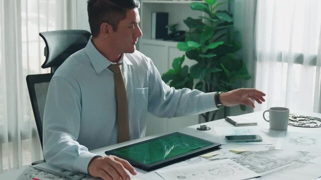 Professional engineer looking at phone while working on tablet with green screen at meeting table with turbine engine or jet engine sketch design and various metal gear scatter around. Alimentation.