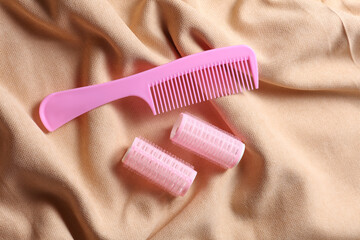 Pink hair curlers and comb on beige velour background