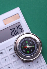 Calculator with number 2025 and compass on green background. Economic analysis, budget of the year
