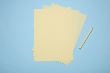 Fototapeta premium Yellow sheets of paper with pencil on blue background