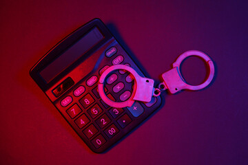 Handcuffs and calculator in red blue neon light. Crime and Justice