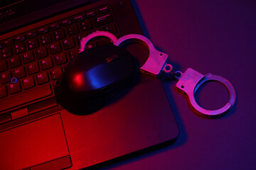 Laptop with handcuffs in neon light. Cyber ​​police
