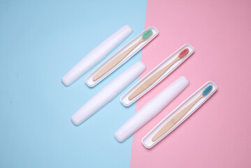 Plastic cases with wooden toothbrushes on blue pink background