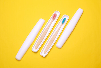Plastic cases with wooden toothbrushes on yellow background