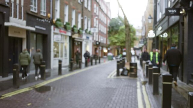 Blurry view of people walking through a cobblestone street in seven dials, london, during autumn with typical uk architecture and defocused shop fronts.