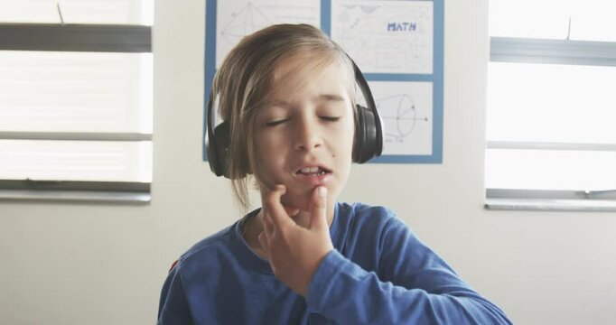 Wearing headphones, boy in school listening to lesson in classroom