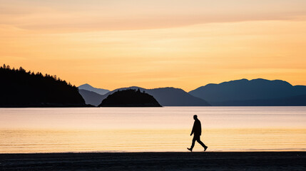 Fototapeta premium Silhouette of lone figure walking on beach at sunset