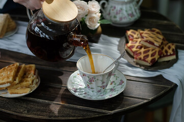 Hands pouring tea from teapot in cozy kitchen during breakfast.