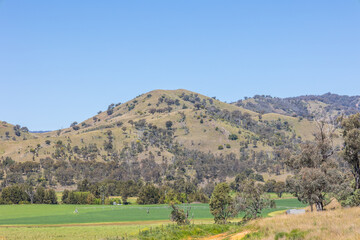 Foothills of the Great Dividing Range with sparse vegetation and a blue sky background, surround...