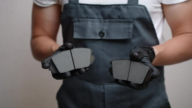 Man in overalls holds and demonstrates two brake pads. Car mechanic is preparing to replace them. Concept car maintenance, serviceability of car brake system.