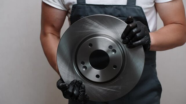 Male auto repairman holds new brake disc in hands, close-up. Auto parts replacement concept, car maintenance, serviceable car brake system.