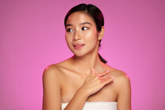 Woman displaying skincare routine with soft expression against pink background during a beauty tutorial session