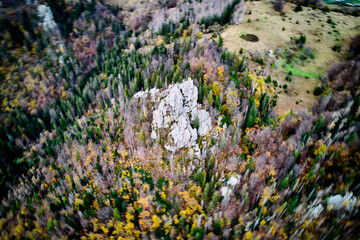 Obraz premium Dynamic aerial view of rocks highlights rugged, rocky outcrop amidst vibrant, autumnal forest. Surrounding landscape, with mix of dense trees and open fields, creates dynamic and colorful scene.