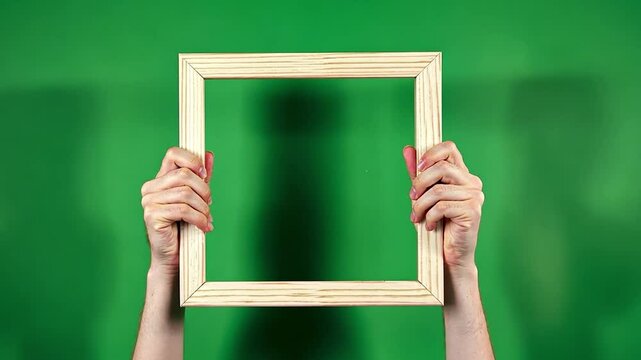 Empty Wooden Frame: Hands delicately hold a simple, empty wooden picture frame against a vibrant green backdrop.  The blurred background hints at potential imagery.