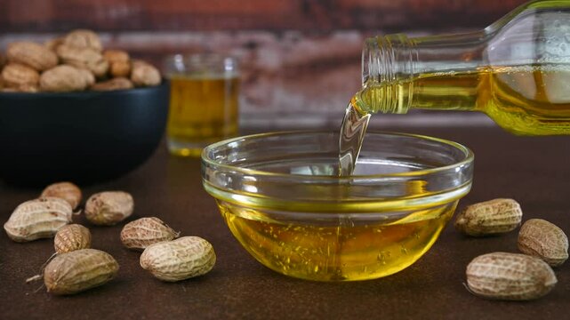 Pouring peanut oil also called as groundnut oil in a cup.