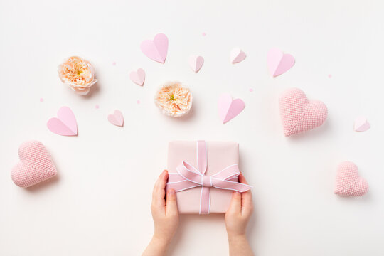 Child hands holding a gift or present box decorated with pink hearts and rose flowers for Happy mothers day. Holiday greting card.