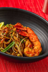 Top view of shrimp Pad Thai with lime in a black bowl