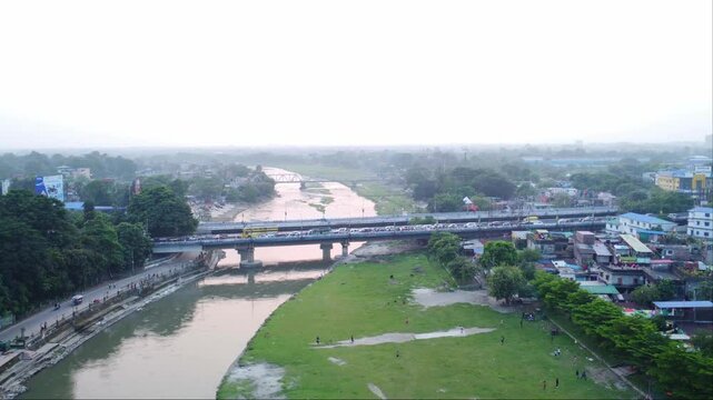 Evening traffic movement over the hill cart road bridge, Mahananda Road bridge over polluted and dirty mahananda river with wastewater open drainage surrounding slum neighborhoods, Siliguri, Drone
