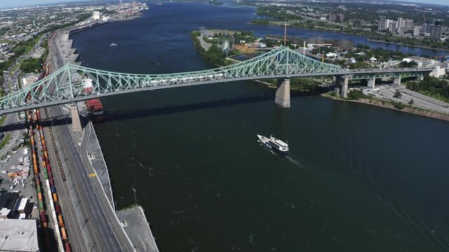 Aerial view of the Jacques Cartier Bridge in Montreal, spanning the St. Lawrence River. Its iconic design and connection between the island and the South Shore, with the city skyline in the backdrop.