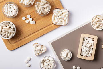 Different dietary supplement pills, minerals and vitamins such as such as vitamin d3, a, e, b, c, magnesium, zinc and calcium in beautiful composition from above on a wooden desk on white background.