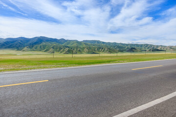 Countryside asphalt road and green meadow with mountain nature landscape on a sunny day. Road trip.