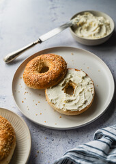 Close up of sesame seed bagel with cream cheese on plate.