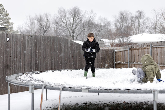 Two kids play in the snow on trampoline in winter
