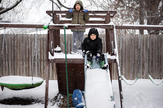 smiling boy about to slide down snowy slide while brother watches