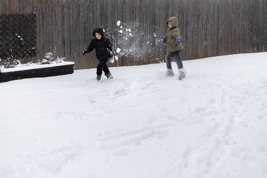 Two kids throwing snowballs and running in a backyard