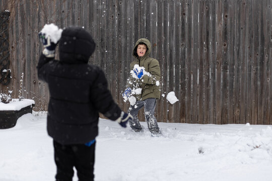 Two kids play in the snow, throwing snowballs in a backyard