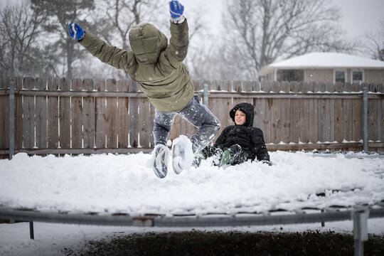 Two kids jumping on a snow-covered trampoline in winter