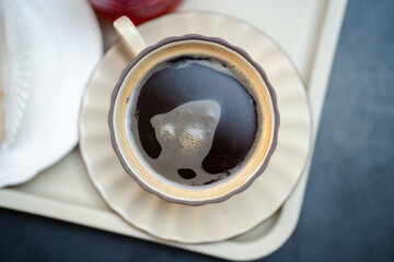 Aerial shot of steaming cup of black coffee in elegant ceramic cup with foam details. Coffee warmth, relaxation and the comforting aroma of fresh brew in morning café.