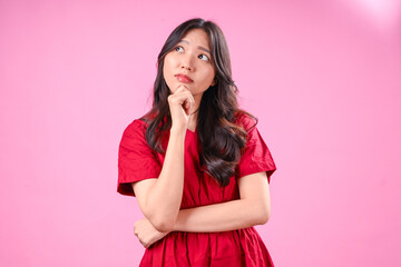 A beautiful young Asian woman with long wavy black hair wears a red dress and looks up thoughtfully...