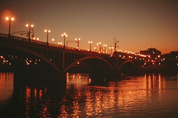 Obraz premium Illuminated Bridge Spanning River at Sunset