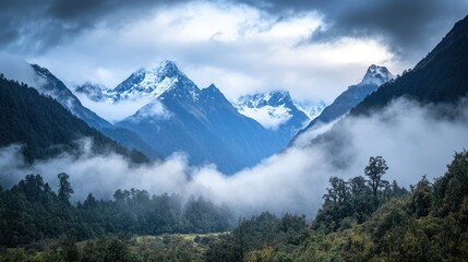 Fototapeta premium A cinematic wide-angle shot of misty mountains with towering, snow-capped peaks, enveloped in thick clouds