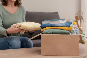 Close up of Woman sitting on sofa and preparing donation box with clothes and items