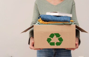 close up of a person holding cardboard box with recycling symbol with items for charity and...