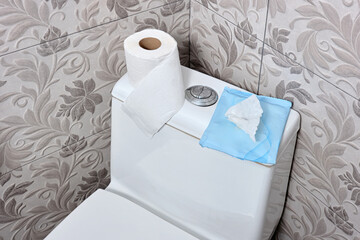 Top view of there roll of toilet paper and wet sanitary wipes lying on the toilet lid in the...