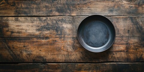 Vacant black circular dish on a rustic dark wood surface viewed from above with natural textures and shades highlighting culinary simplicity