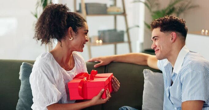 Couple, love and gift on sofa for Valentines day, celebration or romantic gesture in home. Shocked woman, man or box in lounge with birthday surprise, present or relationship milestone with thank you