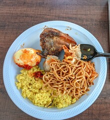 A vibrant plate featuring yellow rice, curry chicken, boiled egg, noodles, and dim sum, creating a colorful and delicious meal.