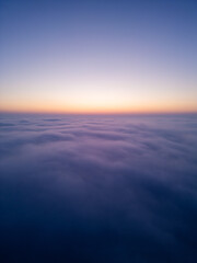 Aerial drone view above clouds at sunrise, high-altitude misty landscape with rolling fog and golden horizon, breathtaking cinematic aerial footage capturing the tranquil beauty of sky and clouds in