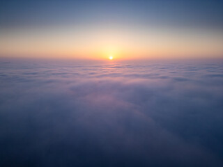 Sunrise above a vast sea of clouds. The golden light gently illuminates the misty sky, creating a dreamlike, tranquil atmosphere with soft colors and smooth motion. Aerial drone view